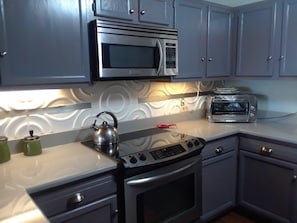 A kitchen with a microwave, toaster, kettle, and stove.