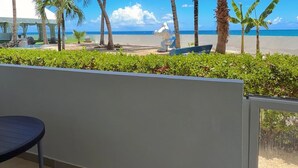 A balcony with a view of the beach, palm trees, and a clear blue sky.