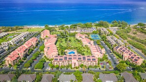 Luchtbeeld van een resort met meerdere gebouwen, een centraal gelegen zwembad en een strand op de achtergrond.