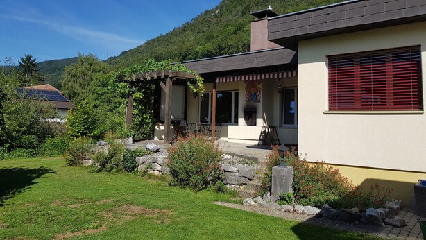 A house with a stone foundation, a wooden pergola, and a stone fireplace. - Holiday home Luma (with terrace and garden) (Egerkingen)