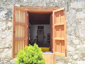 Un edificio de piedra con una puerta de madera abierta, que muestra una habitación con un reloj, una silla y una pequeña mesa.