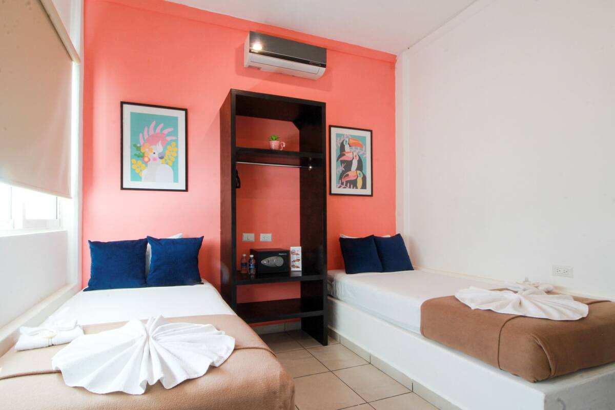 A hotel room with two beds, a wardrobe, and two framed artworks on the walls.