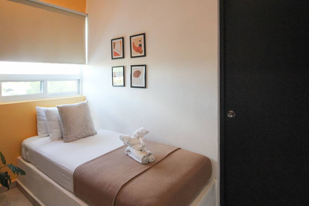 A bedroom with a bed, pillows, a blanket, a small plant, and framed pictures on the wall.