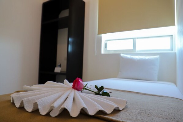 A neatly made bed with a white pillow and a single rose on a white towel.