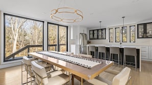 Una cocina moderna con ventanas amplias, una mesa larga para comer y taburetes de bar.