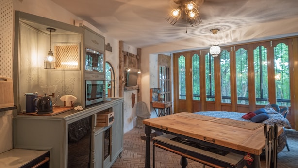 A rustic kitchen with a wooden table, a sink, and a window overlooking greenery.