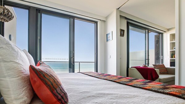 A modern bedroom with a large bed, a view of the sea, and a balcony.