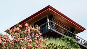 Un edificio moderno con techo rojo, balcón y plantas florecientes de color rosa al frente.