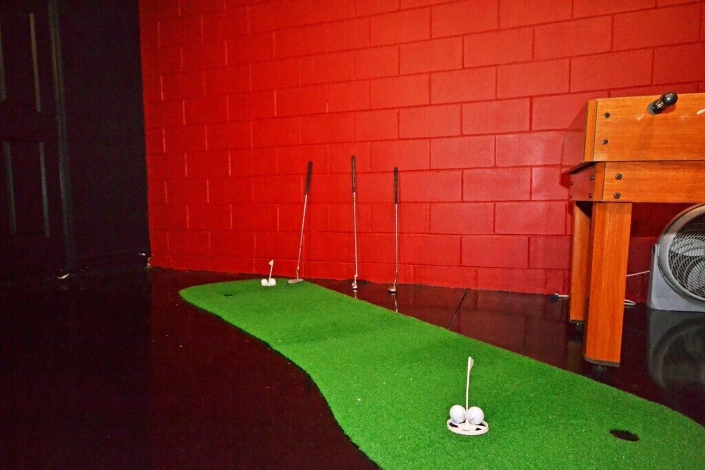 A room with a red brick wall, a green carpet, and a wooden table with a fan.
