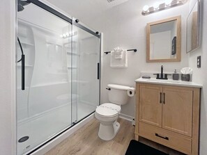 Une salle de bain moderne avec une douche à parois de verre, des toilettes et un meuble-lavabo en bois doté d’un miroir.
