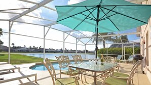 A covered outdoor area with a pool, dining table, chairs, and a large umbrella.