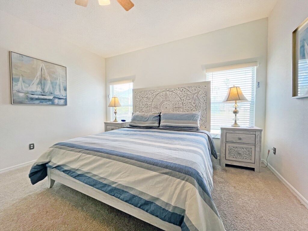A bedroom with a large bed, two bedside tables with lamps, a decorative headboard, and a painting of sailboats on the wall.