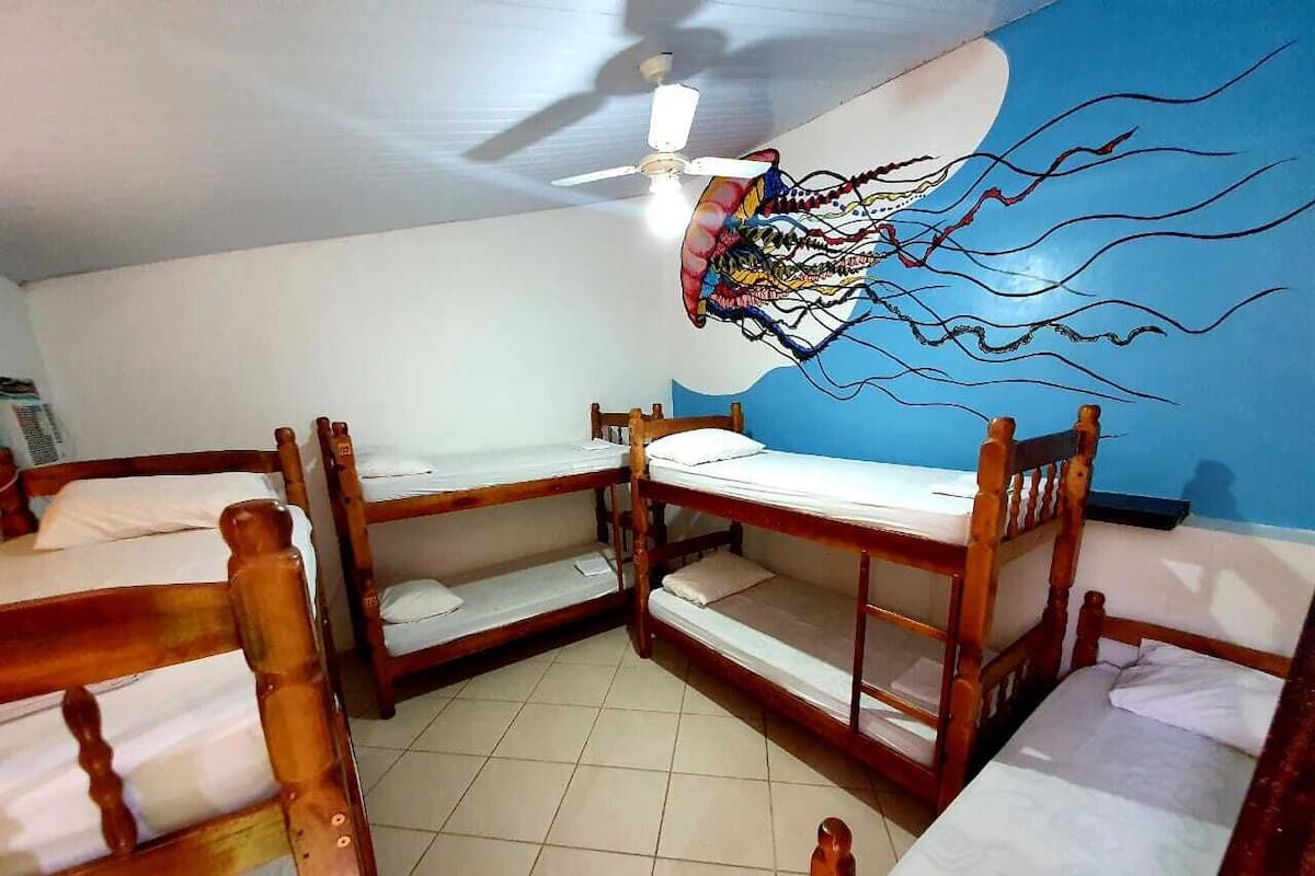 Une chambre avec des lits superposés, un ventilateur de plafond et une fresque murale.