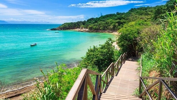 A wooden boardwalk leading to a beach with clear turquoise water and lush greenery. - Hostel Minha Lua (Búzios)