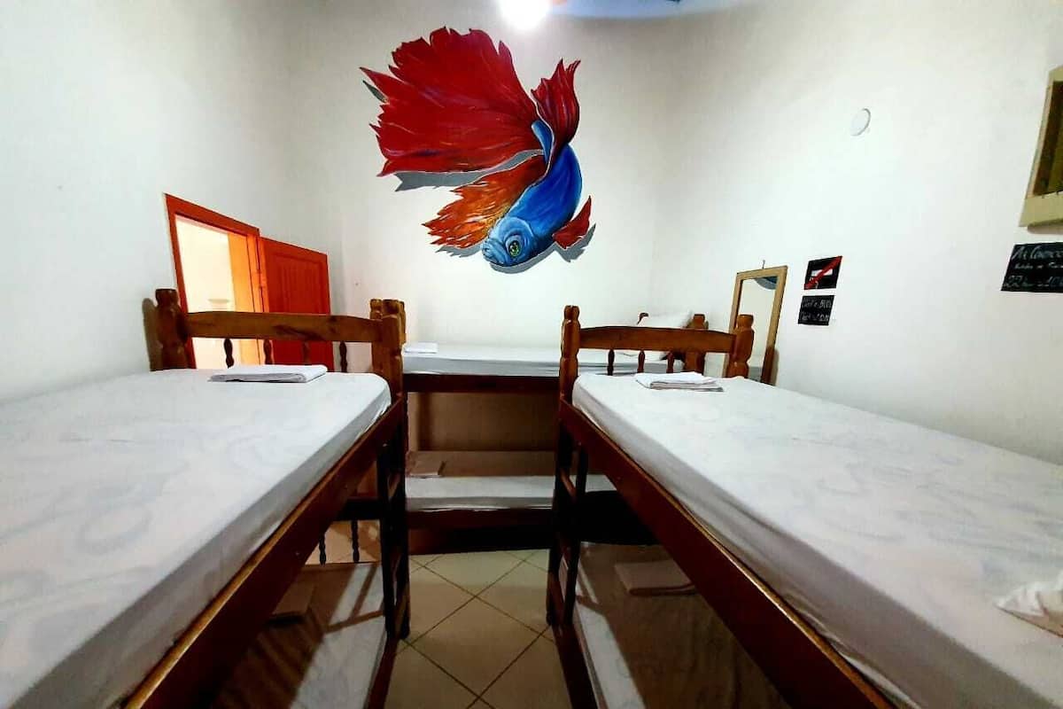 Une pièce avec deux lits superposés en bois, une petite table et une fresque murale représentant un poisson.