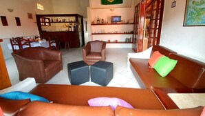 A spacious living area with leather sofas, a coffee table, and a television. A Brazilian flag is visible on the wall, and there is a bar area in the background. - Hostel Minha Lua (Búzios)