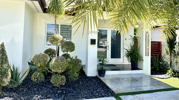 A modern house with a well-maintained garden, a palm tree, and a 'WELCOME' sign.