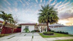 A residential house with a paved driveway, a palm tree, and a fenced yard.