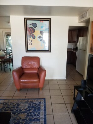 A living room with a brown leather chair, a framed abstract painting, a blue patterned rug, and a television on a stand. - Tucson Delight (Tucson)
