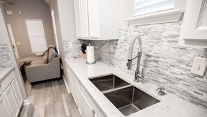 Una cocina moderna con armarios blancos, encimera de granito y salpicadero de piedra.