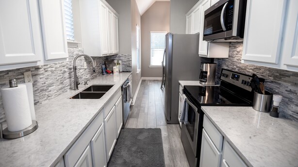 Una cocina moderna con armarios blancos, un refrigerador de acero inoxidable, un microondas y una estufa.