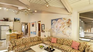 A spacious living room with a large patterned sofa, a dining area with a table and chairs, and a kitchen area with cabinets and a refrigerator.