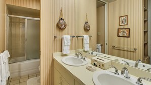 A bathroom with striped wallpaper, a large mirror, two sinks, a shower, and towels hanging on a rack.