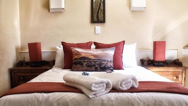 Een opgemaakt bed met een wit en rood kleurenschema, een decoratief kussen en een opgevouwen handdoek op het bed.