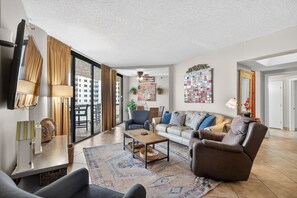 Amplia sala de estar con sofá, sillón y mesa de centro, ventanas grandes y vista a la ciudad.