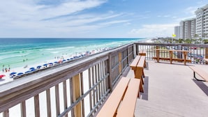 Uitzicht op het strand vanaf een balkon met houten leuningen, een houten terras en een zicht op de oceaan en mensen op het strand.