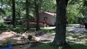 A cabin with a red roof, surrounded by trees and a gravel path.