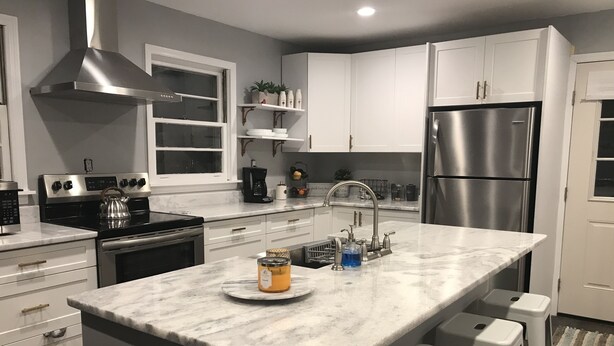 A modern kitchen with white cabinets, stainless steel appliances, a marble countertop, and a built-in island with stools.