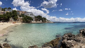Una platja costanera amb aigües cristal·lines, un litoral rocos i edificis al fons.