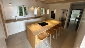 Una cuina moderna amb una illa central, tamborets de bar, llums penjants i forn integrat.