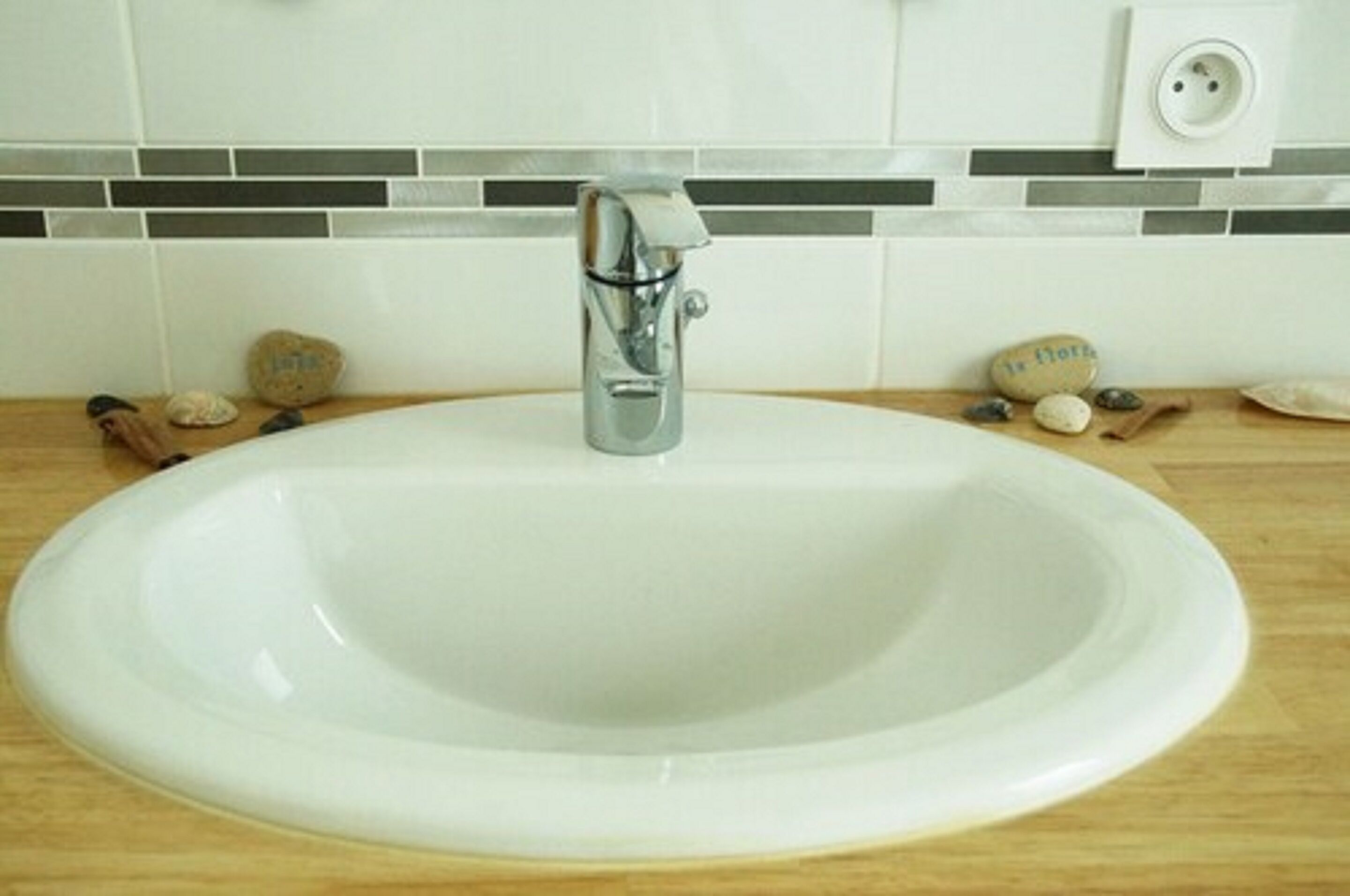 A white ceramic sink with a modern faucet, set against a tiled backsplash with a gray and white pattern.