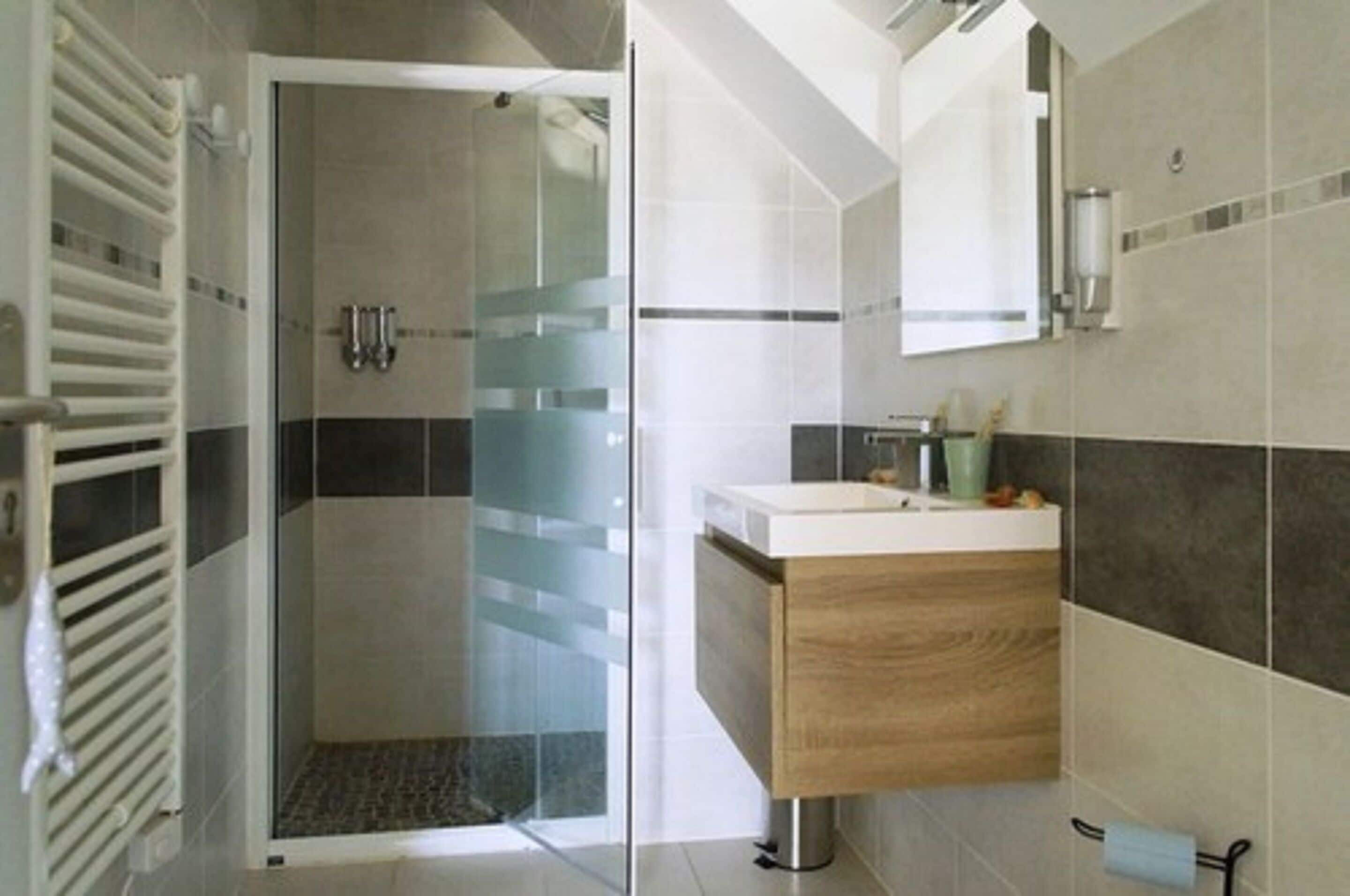 A modern bathroom with a glass shower enclosure, a wooden vanity, and a tiled backsplash.