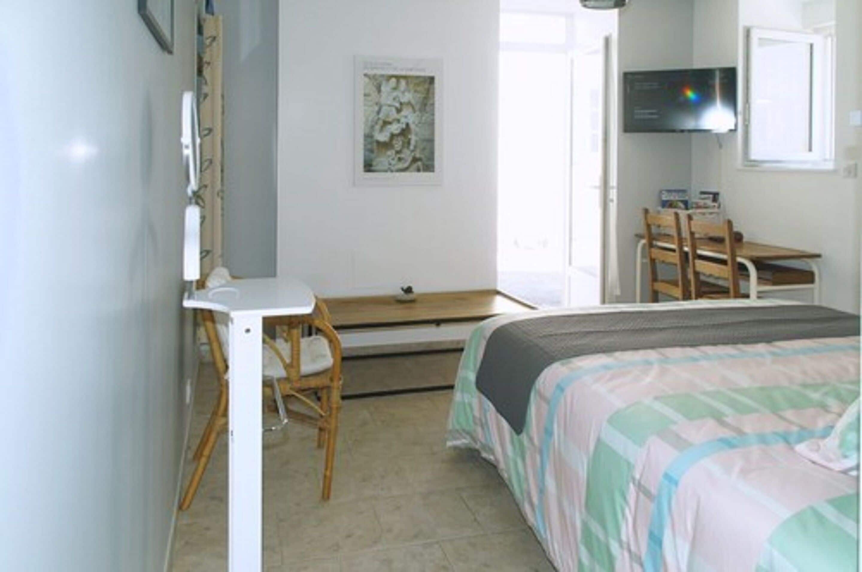 Un dormitorio con cama, escritorio, silla, televisor y ventana.