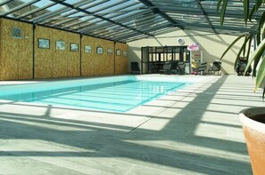 An indoor swimming pool with a glass ceiling and tiled floor, surrounded by walls with framed pictures. - Best Saintonge (Port-d'Envaux)