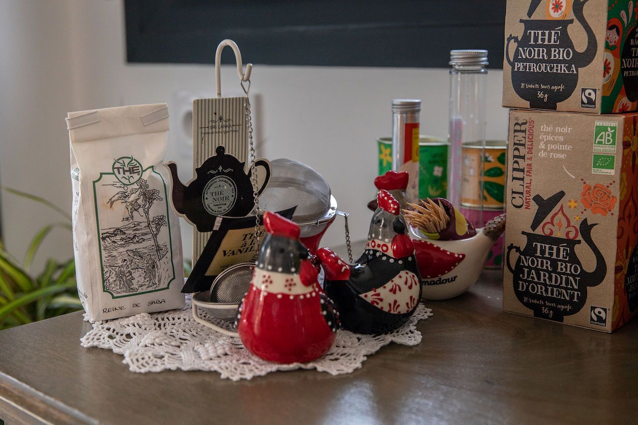 A table with kitchen items including a coffee bag, a strainer, a teapot, and decorative salt and pepper shakers.