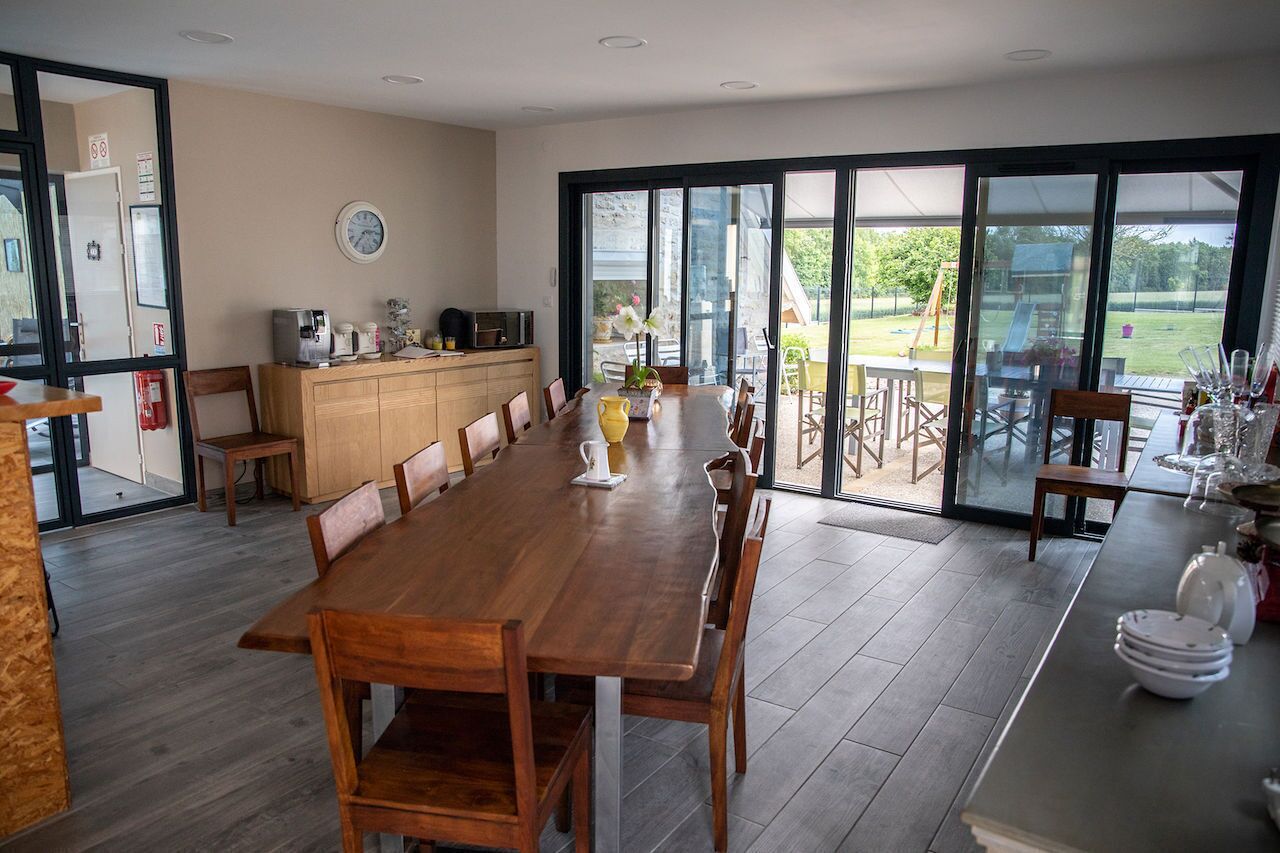 Un comedor moderno con una mesa y sillas de madera, una barra de cocina con electrodomésticos y grandes puertas correderas de vidrio que dan a un patio exterior.