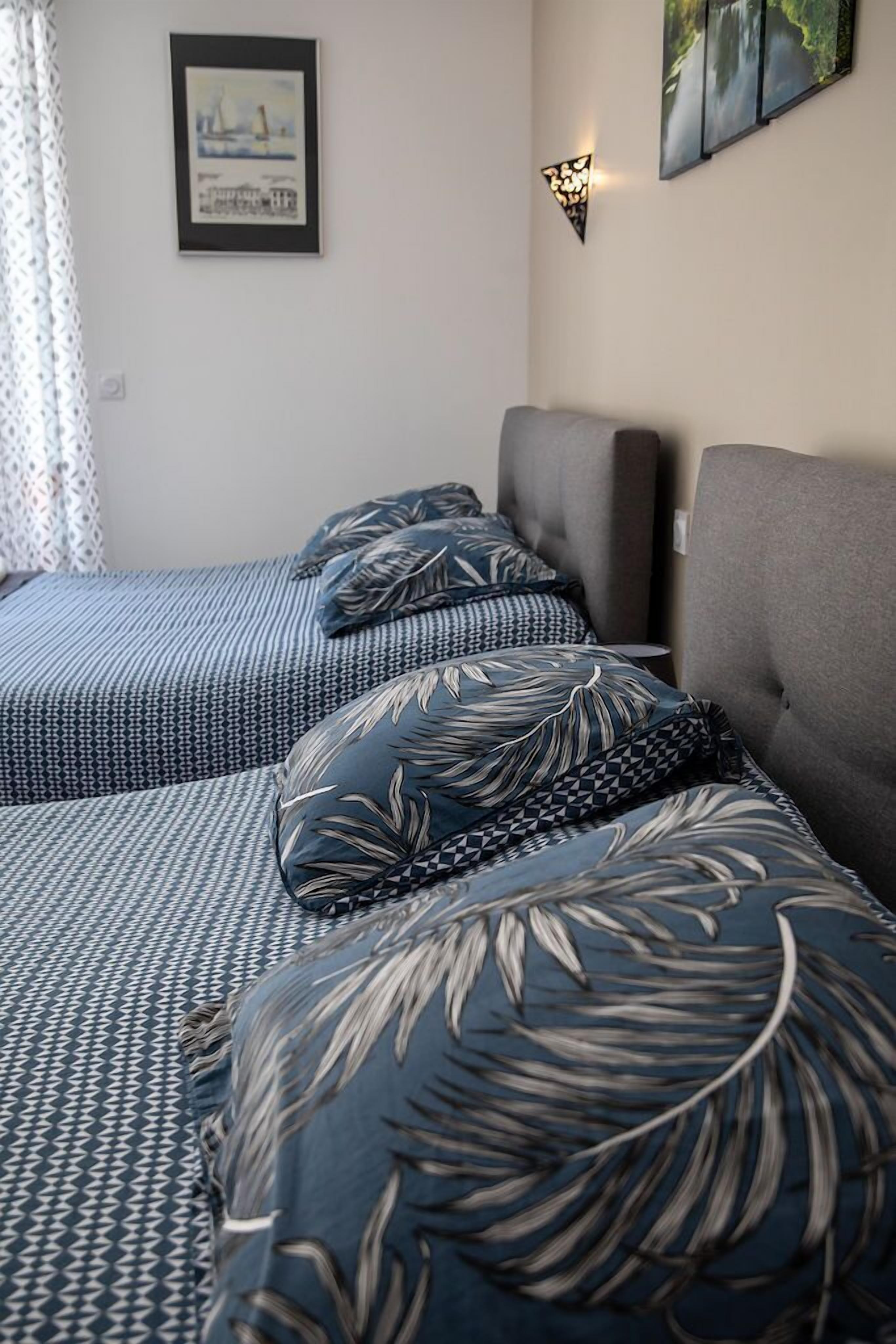 Ett hotellrum med två sängar, båda med mönstrat sänglinne och matchande kuddar. På väggen hänger en inramad tavla och det finns en väggmonterad lampa.