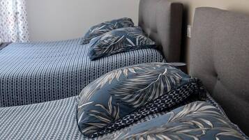 Ett hotellrum med två sängar, båda med mönstrat sänglinne och matchande kuddar. På väggen hänger en inramad tavla och det finns en väggmonterad lampa.