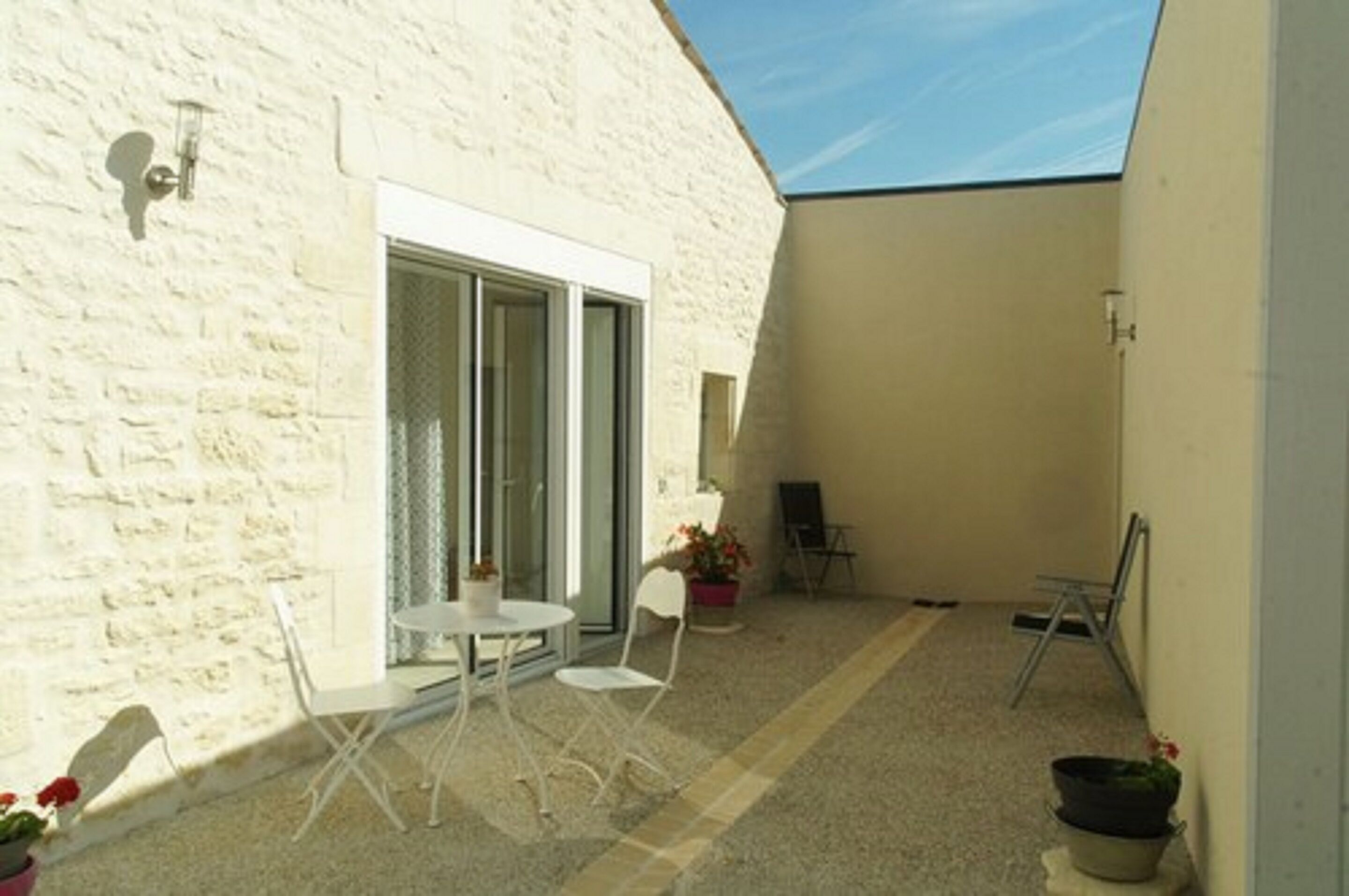 A small, enclosed patio area with a white table and chairs, a sliding glass door, and a few potted plants.