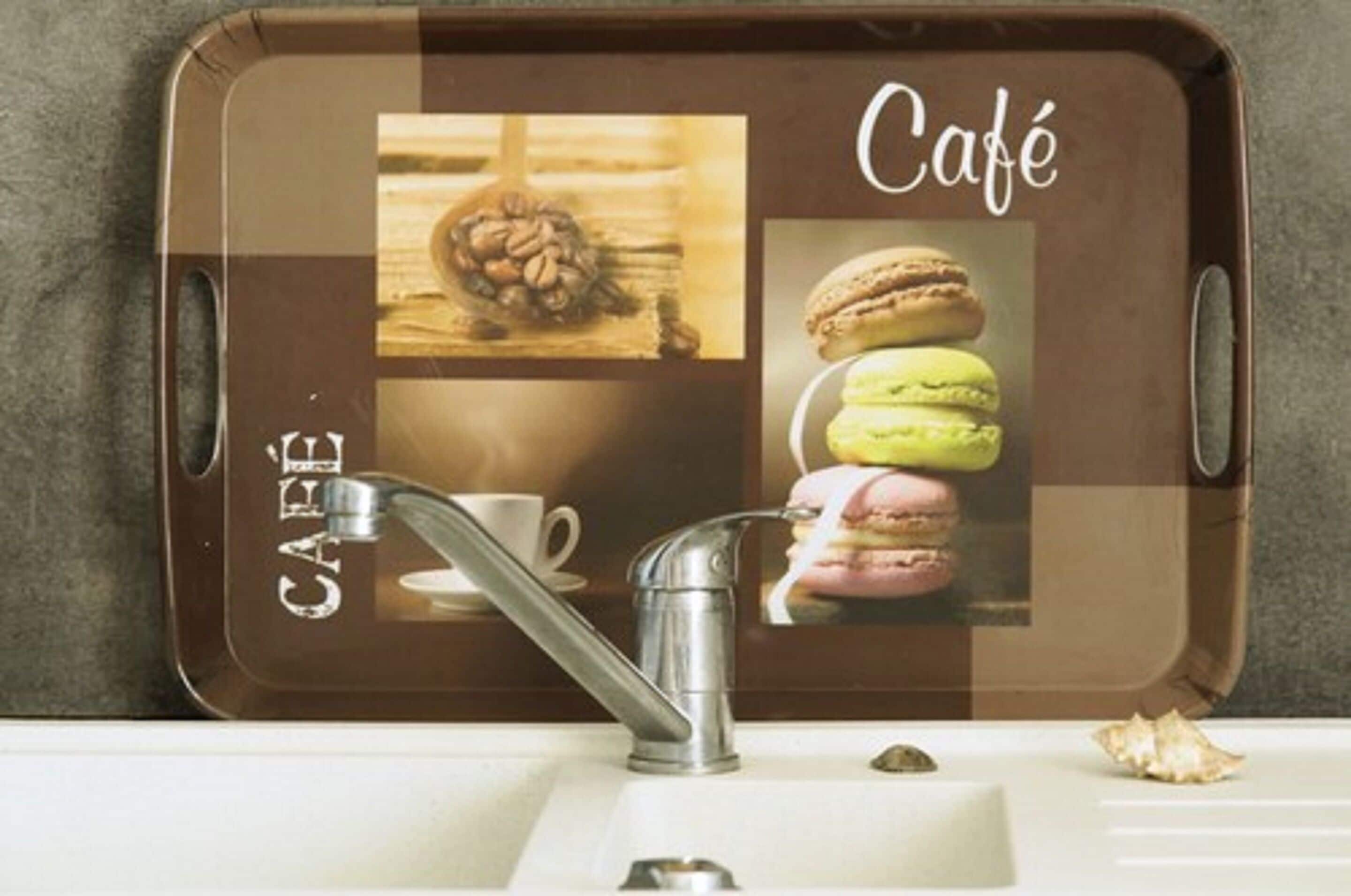 Una encimera de cocina con una cafetera, una taza de café y una bandeja con imágenes de granos de café y macarons.