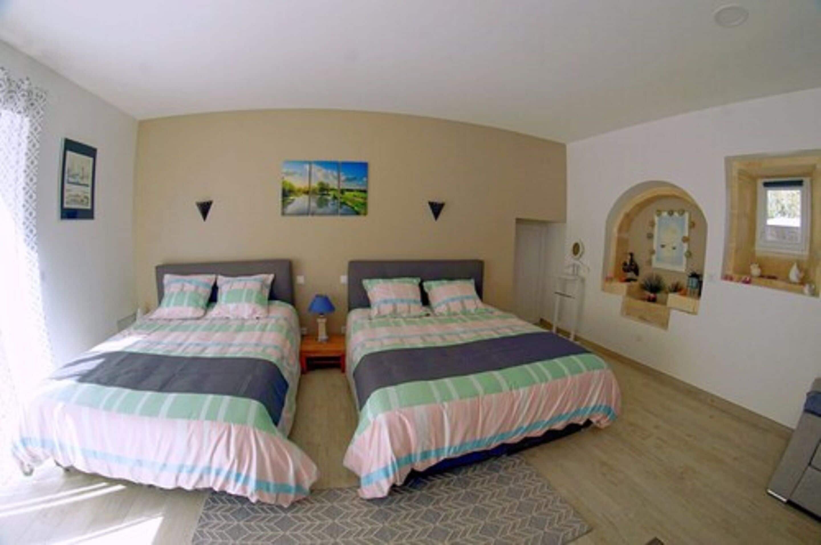 Een slaapkamer met twee bedden, een nachtkastje, een lamp, een spiegel en een raam.