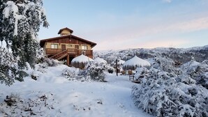 Un chalet en bois doté d’un balcon, entouré d’arbres et de collines couverts de neige.