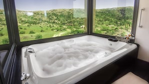 Une salle de bain avec une grande baignoire remplie de mousse, une fenêtre donnant sur un paysage verdoyant et un plafond en bois.