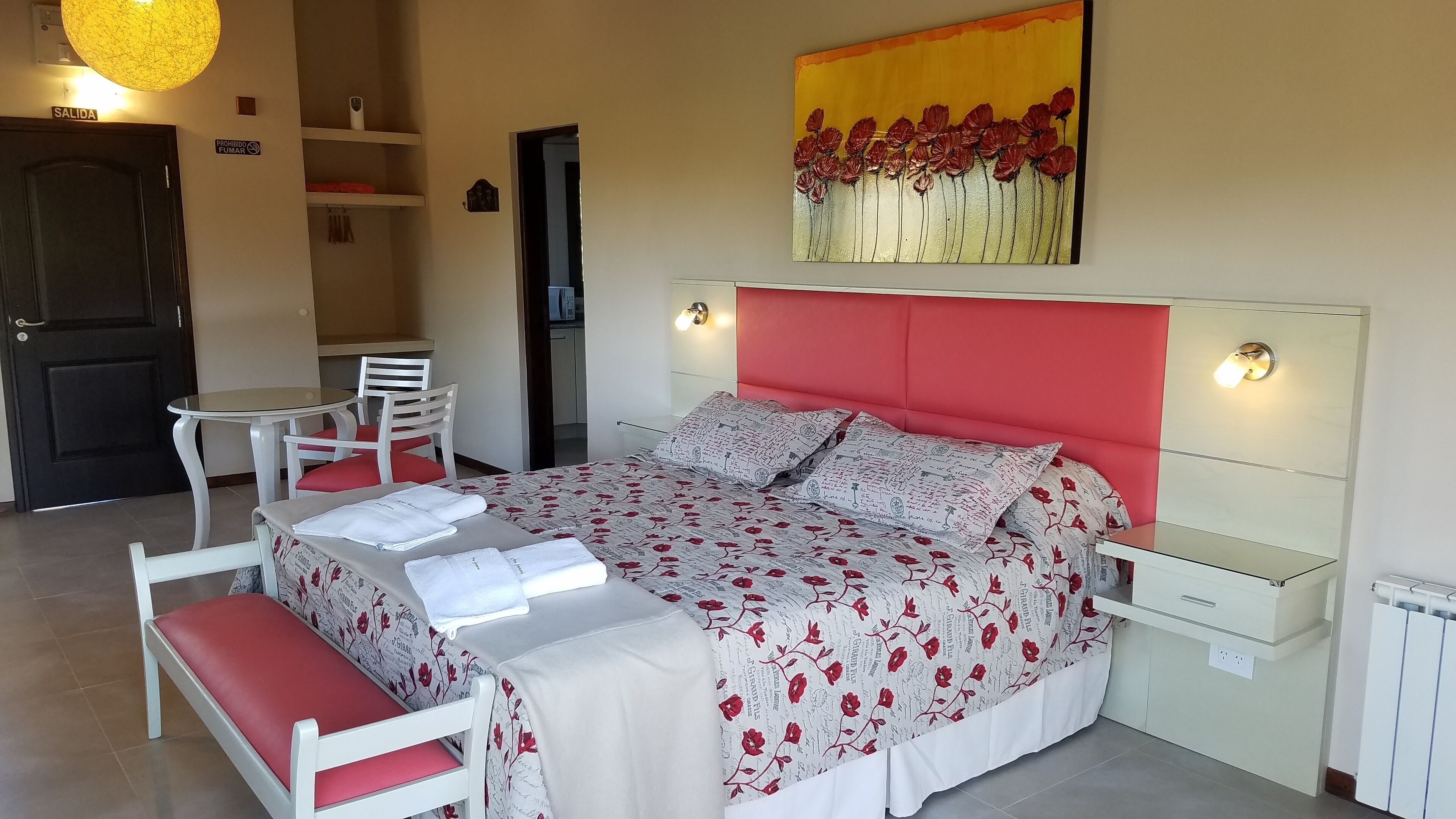 Un dormitorio con cama, mesitas de noche, un escritorio, sillas y un cuadro en la pared.