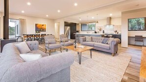 A modern living room with a sofa, armchairs, and a coffee table. There is a kitchen area with a stove and a dining table. - Piper—Family Retreat in the Heart of Wine Country (Wilyabrup)