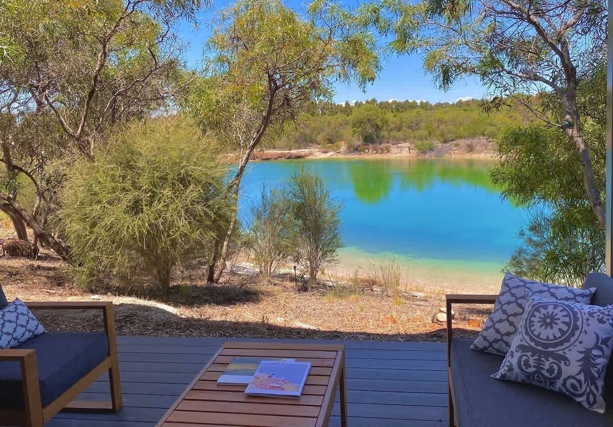 A wooden deck with two chairs and a table, overlooking a calm lake with a clear sky.